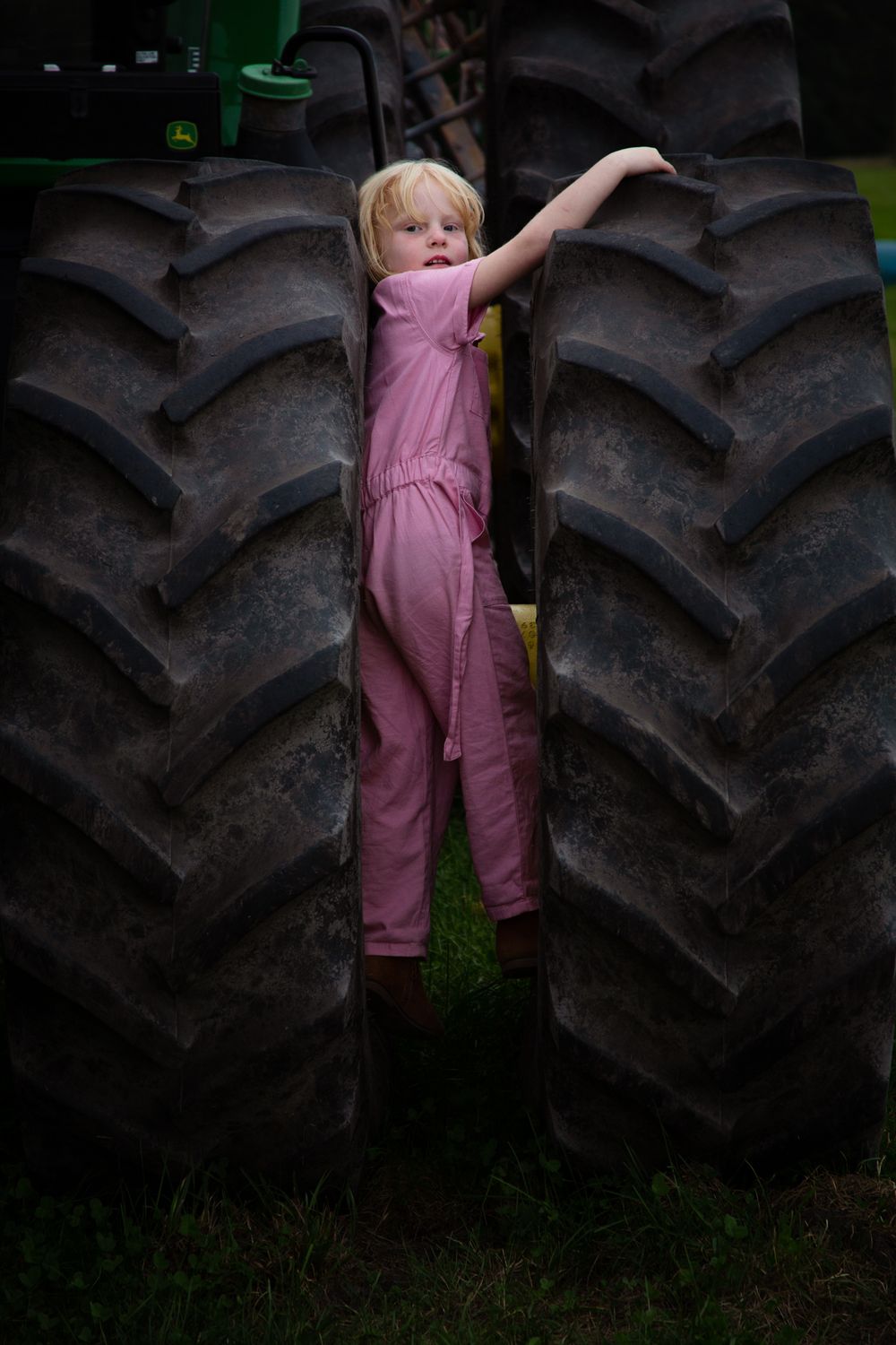 Child in pink overalls exploring near large tractor tires.