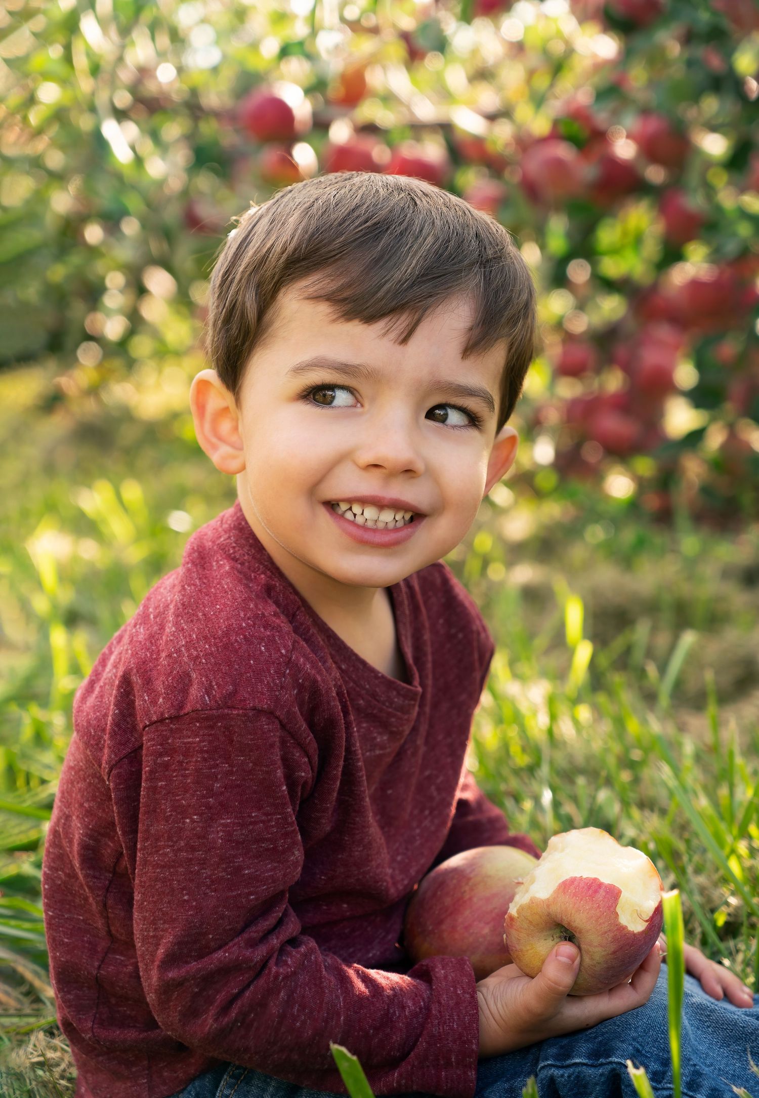 boy smiles playfully with lap full of apples