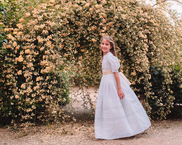 Young girl in white dress twirling through garden with blooming flowers.