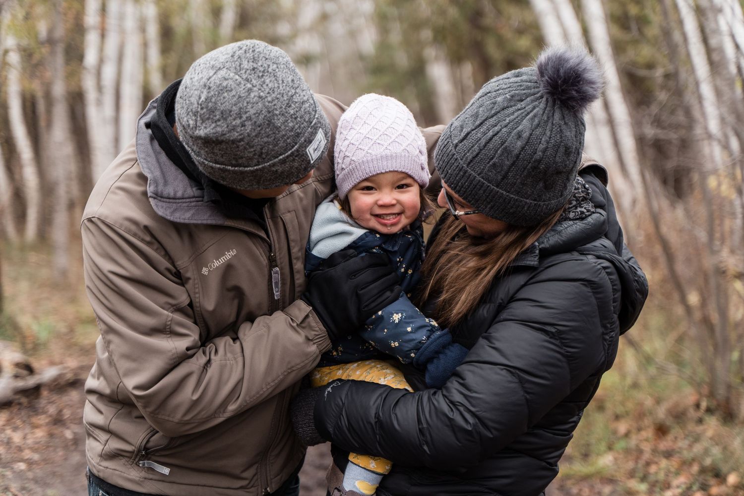 Family of parents and child snuggle together on a trail in the west end of Ottawa in late fall.