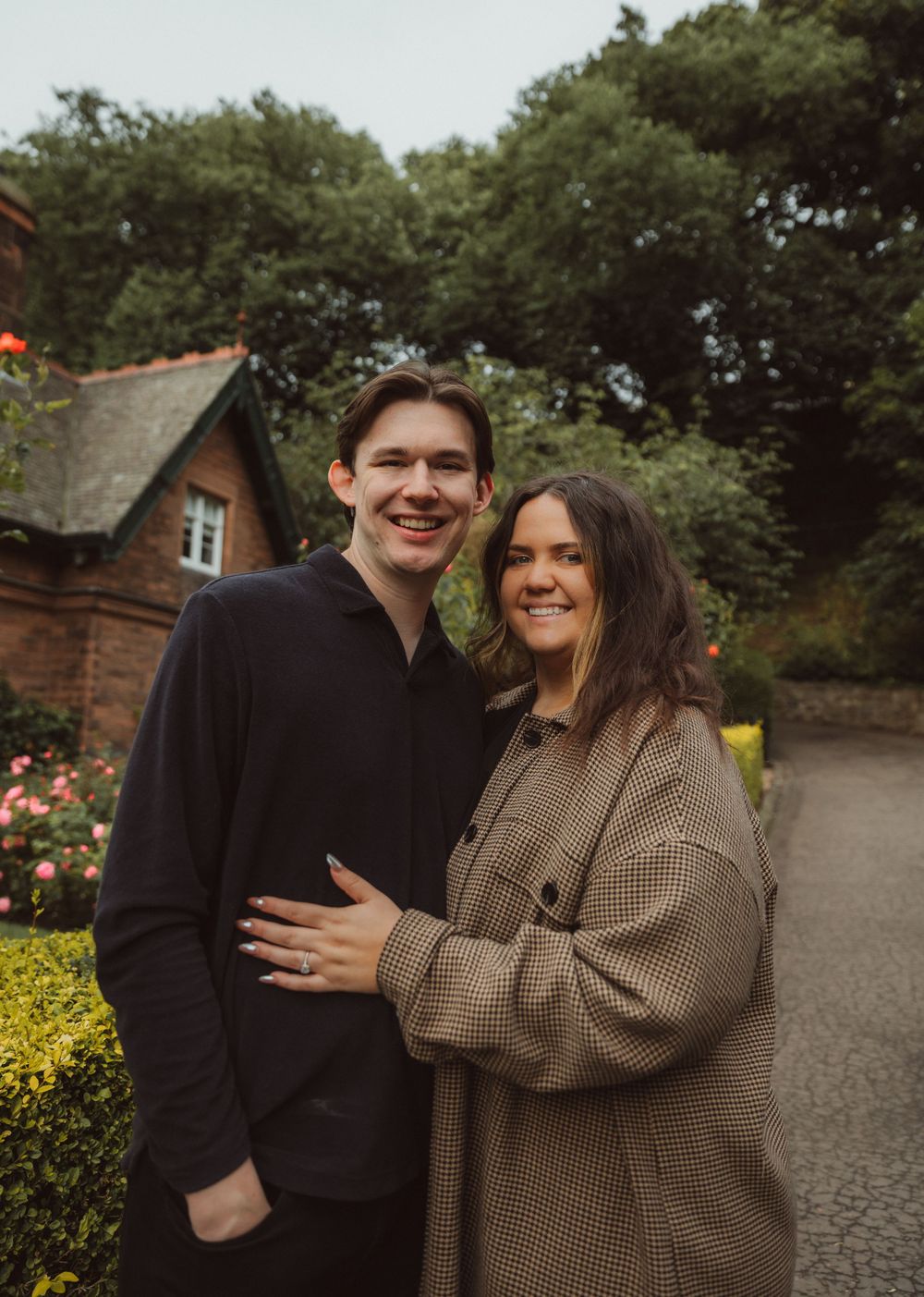 Happy couple embraces outside brick cottage with blooming garden.