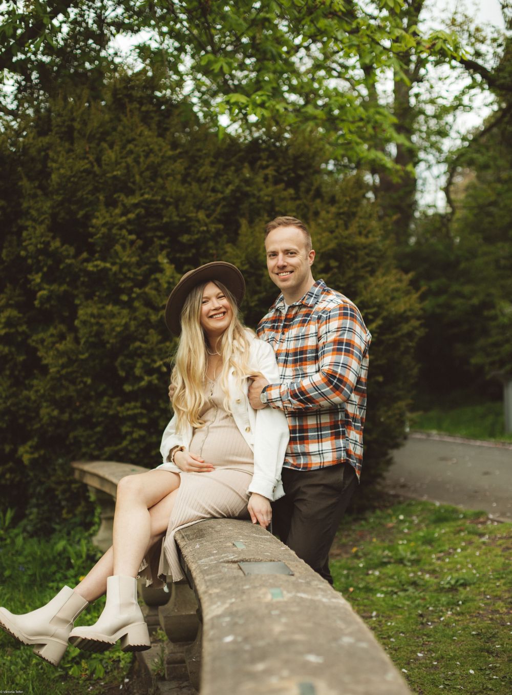 Casual couple sitting together on a stone wall in a park setting.