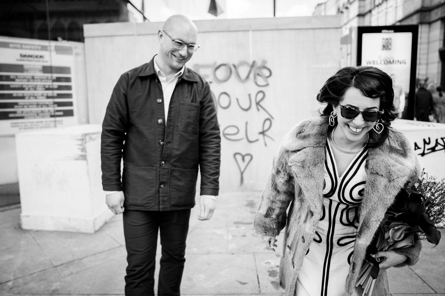 Street style portrait of two people standing in front of urban graffiti wall.