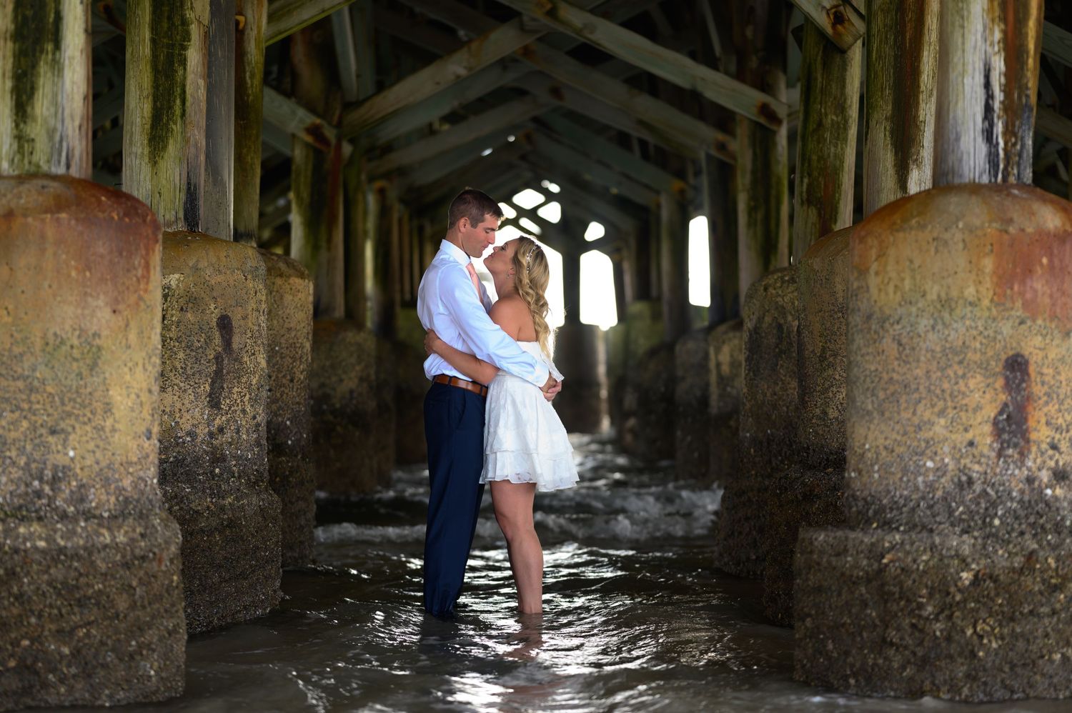 Bride and Groom stand under pier.
