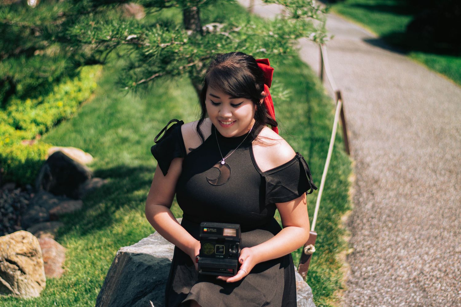 Photographer in black outfit smiling while holding camera in garden setting.