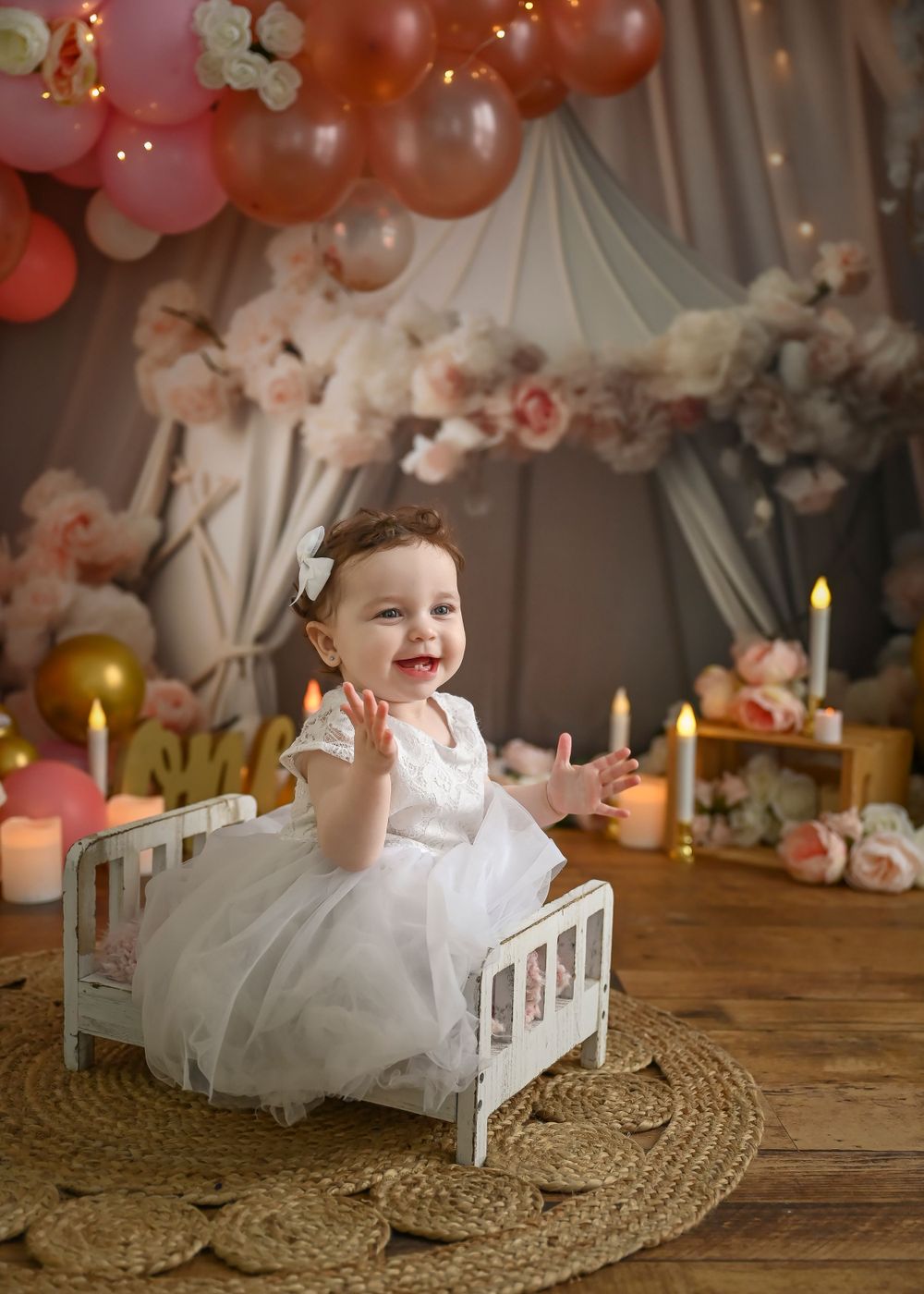 A festive setting with a white crib, pink and orange balloons, and floral decorations against a draped backdrop.