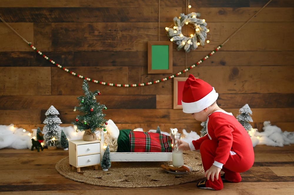 A Christmas scene with wrapped presents, miniature trees, and string lights against a rustic wooden wall.