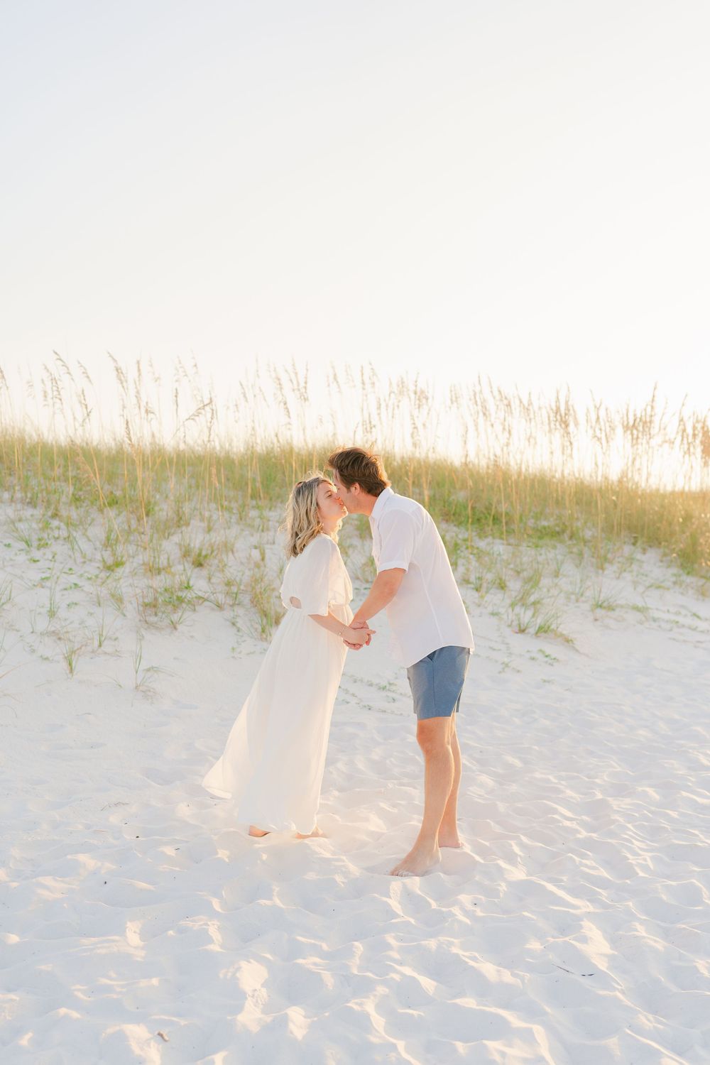 Romantic beach scene with couple embracing in sand dunes during golden hour.