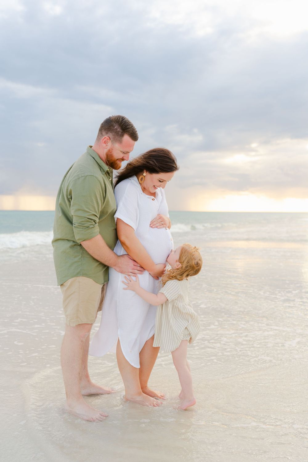 Family shares intimate moment together on beach at sunset.