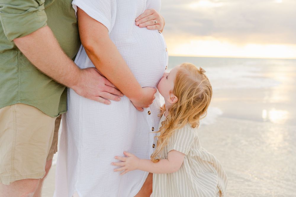 Close-up of family embracing on beach with focus on pregnant belly.
