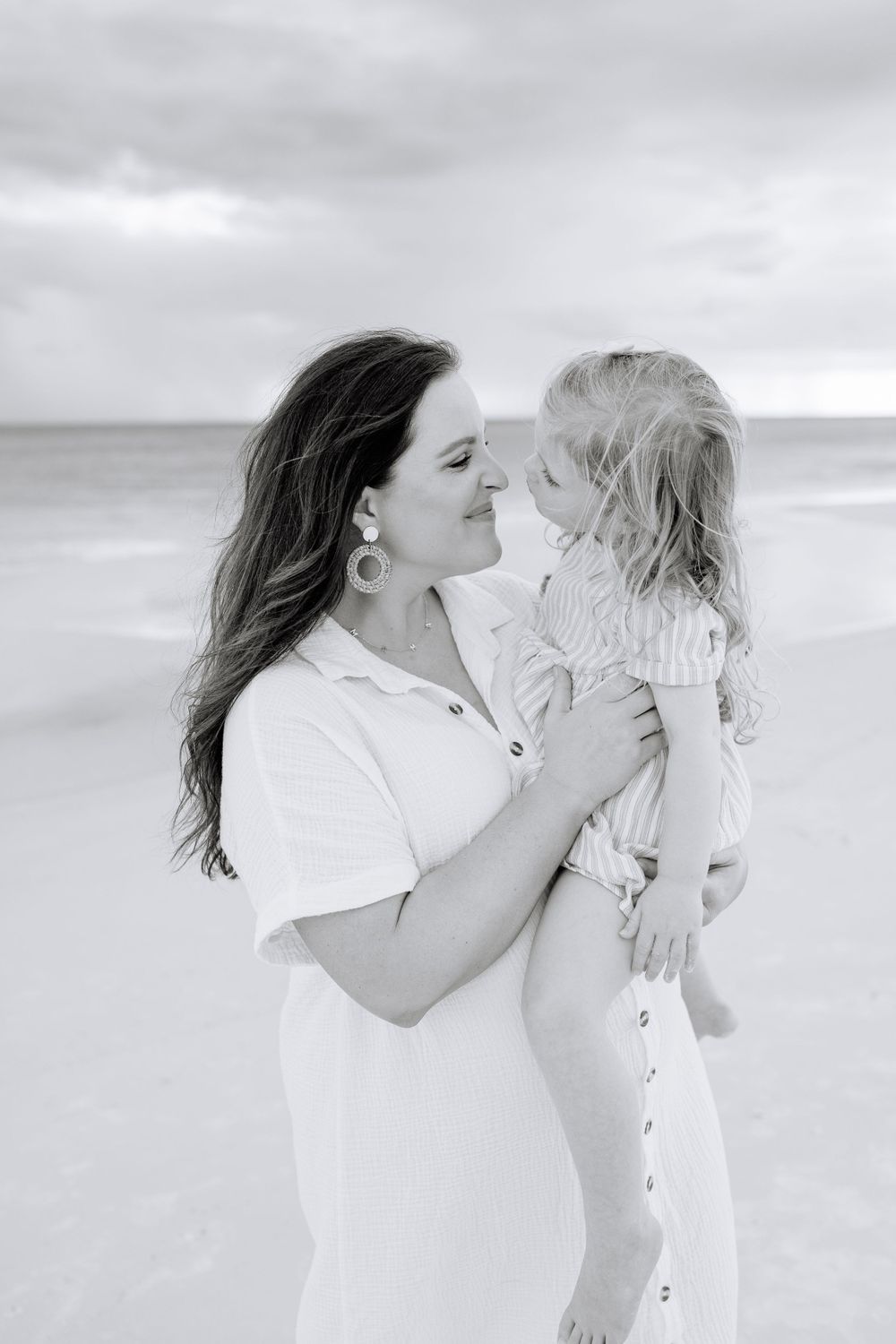 Black and white portrait of mother and child sharing intimate moment on beach.
