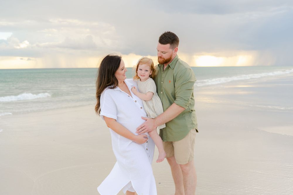 Family shares tender moment on sandy beach at dusk wearing coordinated white and green outfits.