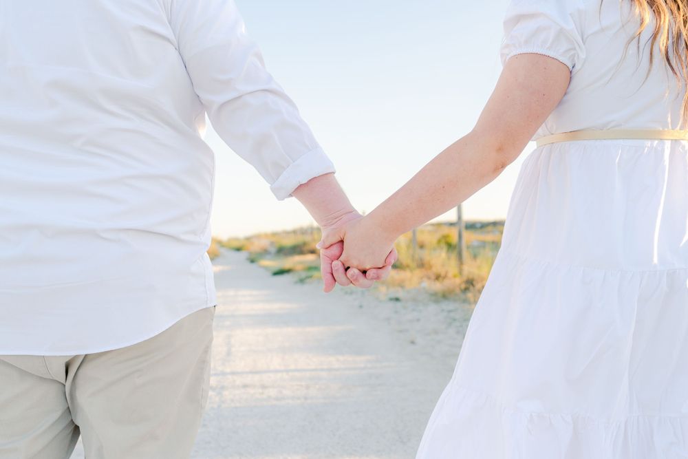 Close-up of couple holding hands on beach at sunset.