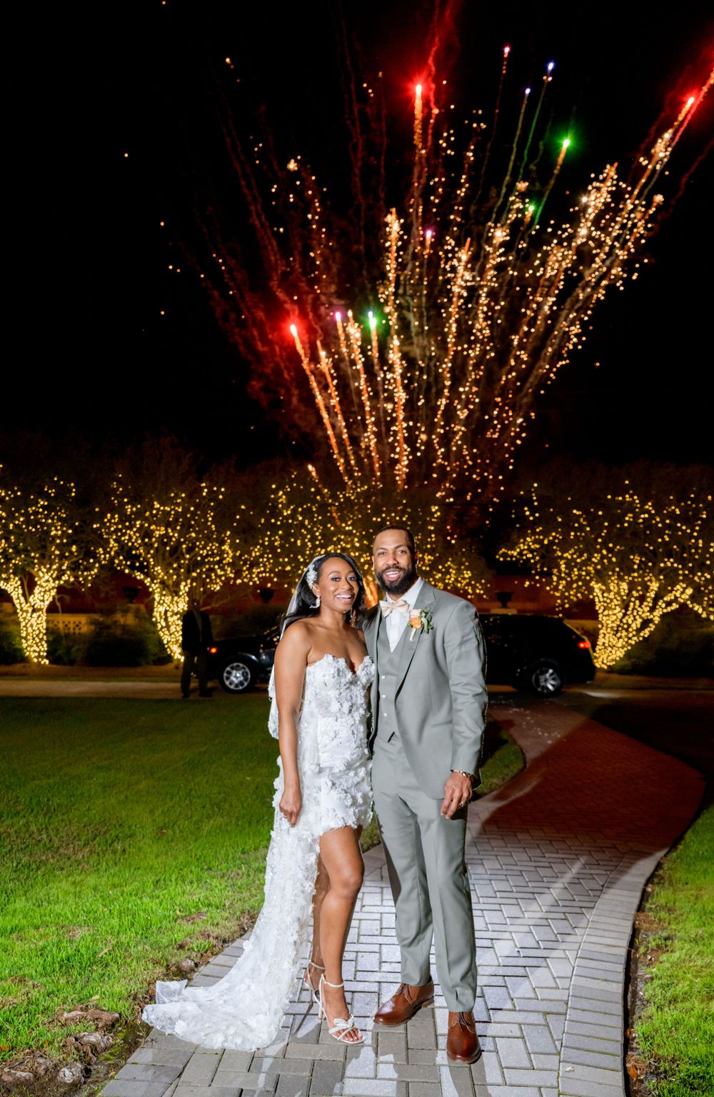 Stunning nighttime wedding portrait with fireworks bursting in golden lights behind the newlyweds.