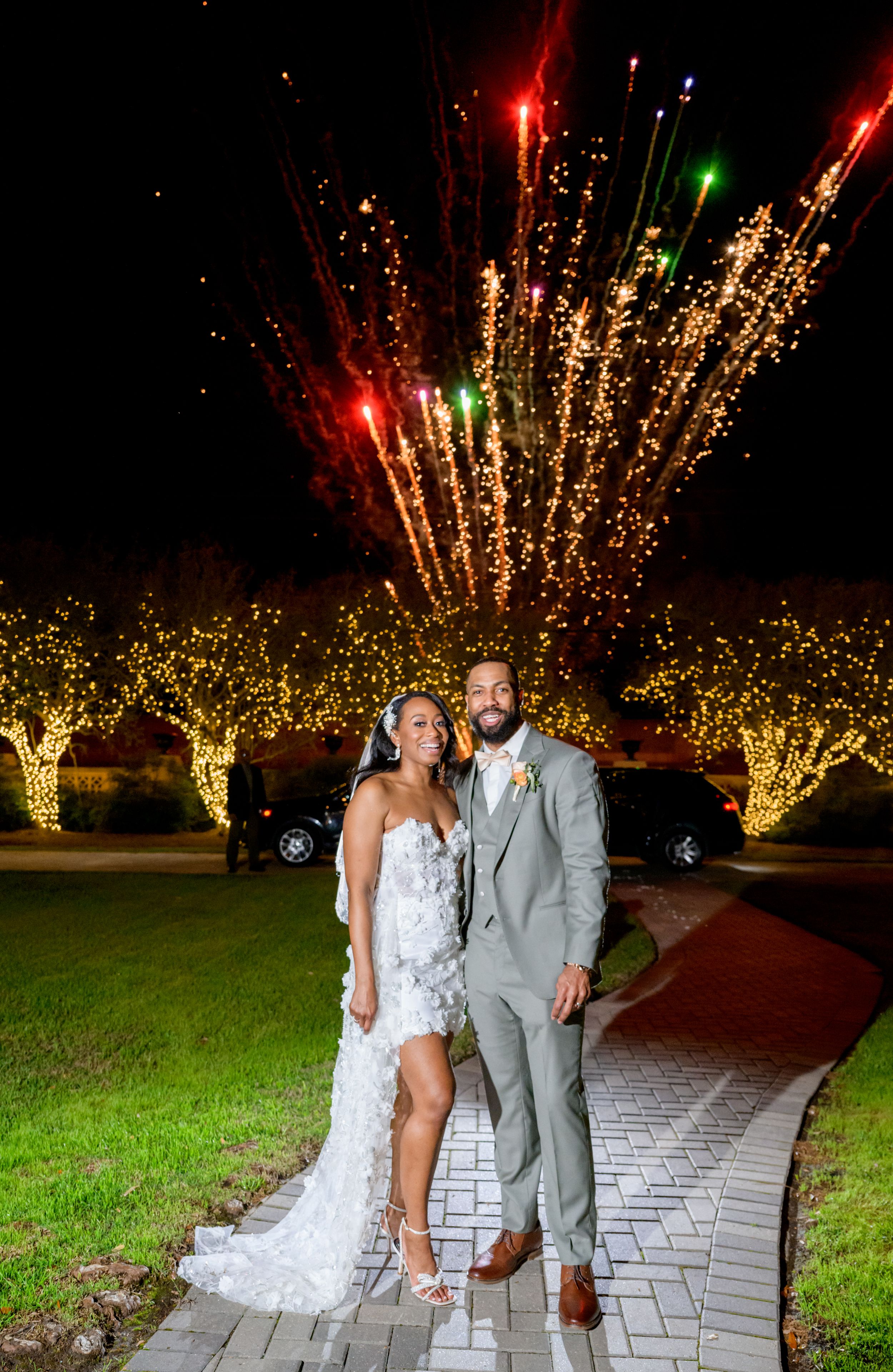 Stunning nighttime wedding portrait with fireworks bursting in golden lights behind the newlyweds.