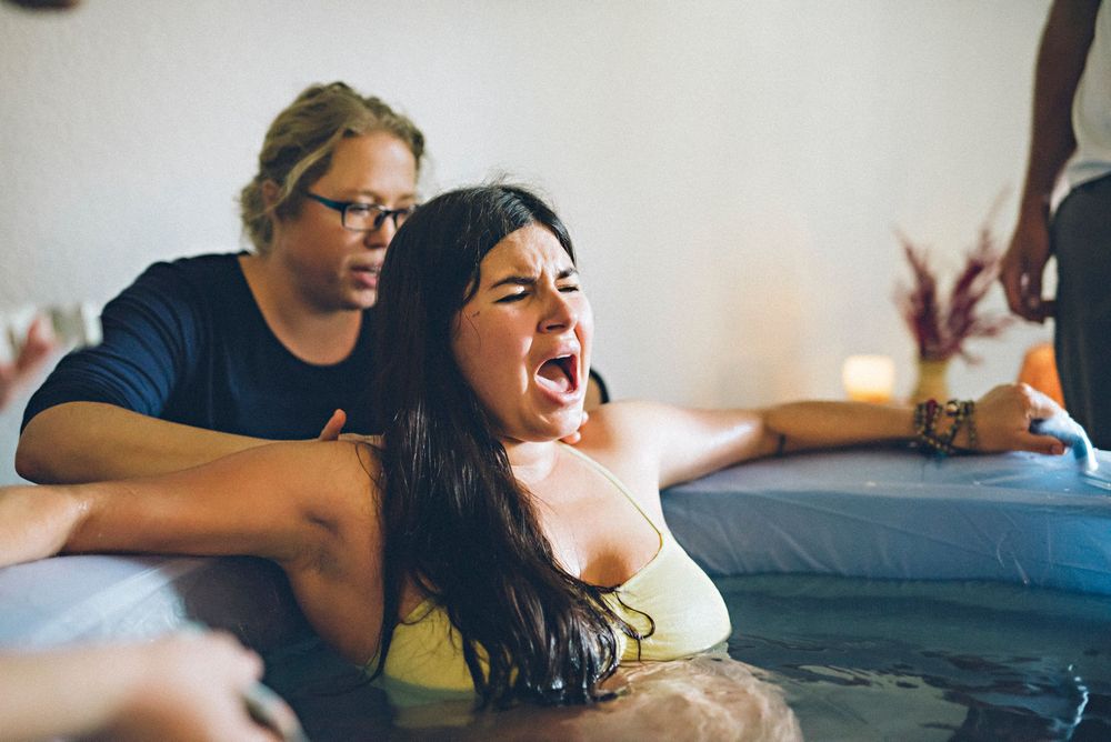 A group of people sit on a couch watching TV and reacting with excitement and laughter.