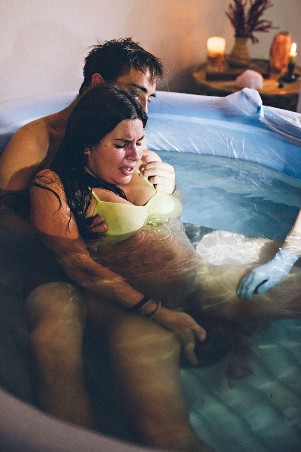 A person labors in a birthing pool during water birth, supported by medical professionals in a dimly lit room.