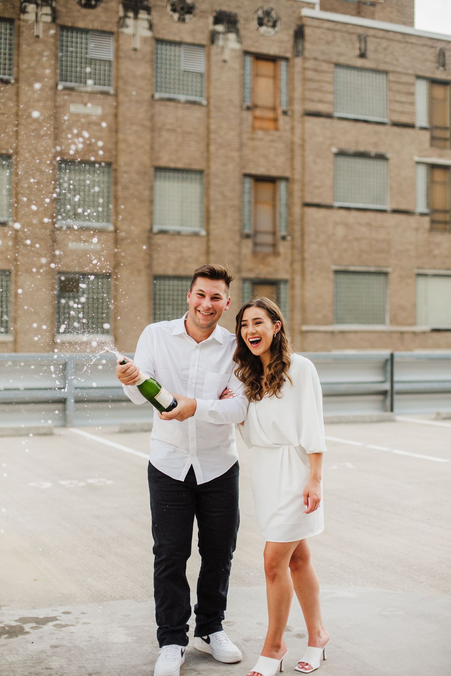 A man pops a bottle of champagne on an urban rooftop. Their STL photographer captures his fiancee laughing next to him.