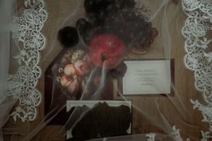 Vintage still life painting displayed with lace fabric and a small card on a wooden surface.