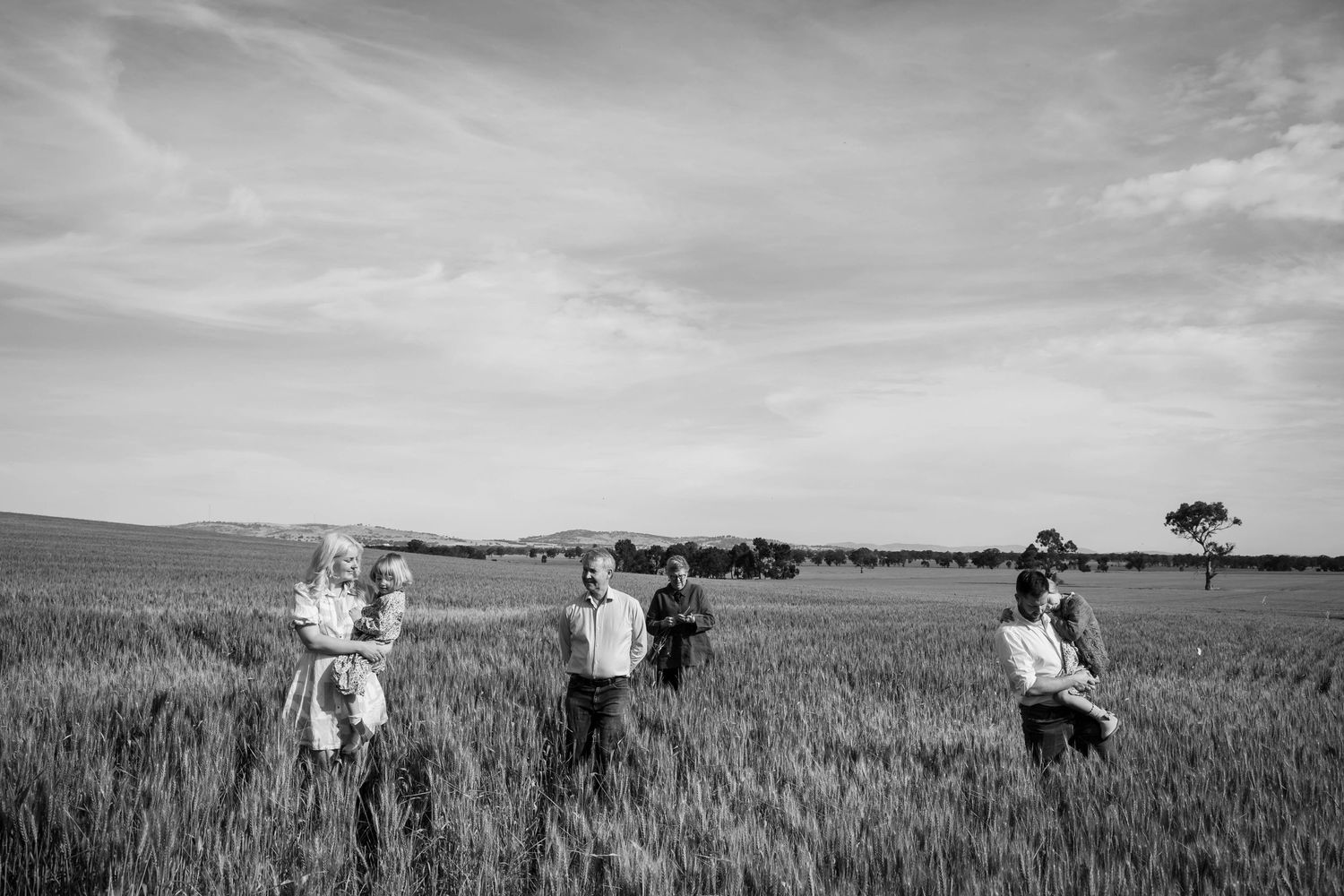 A black and white photograph of people running through a sunlit wheat field on a cloudy summer day.