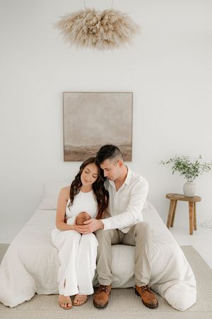 Couple sitting on a bed holding their newborn baby in a photography studio in Jacksonville