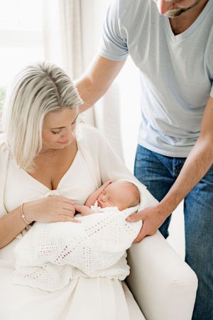 Couple sitting on a bed holding their newborn baby in a photography studio in Jacksonville