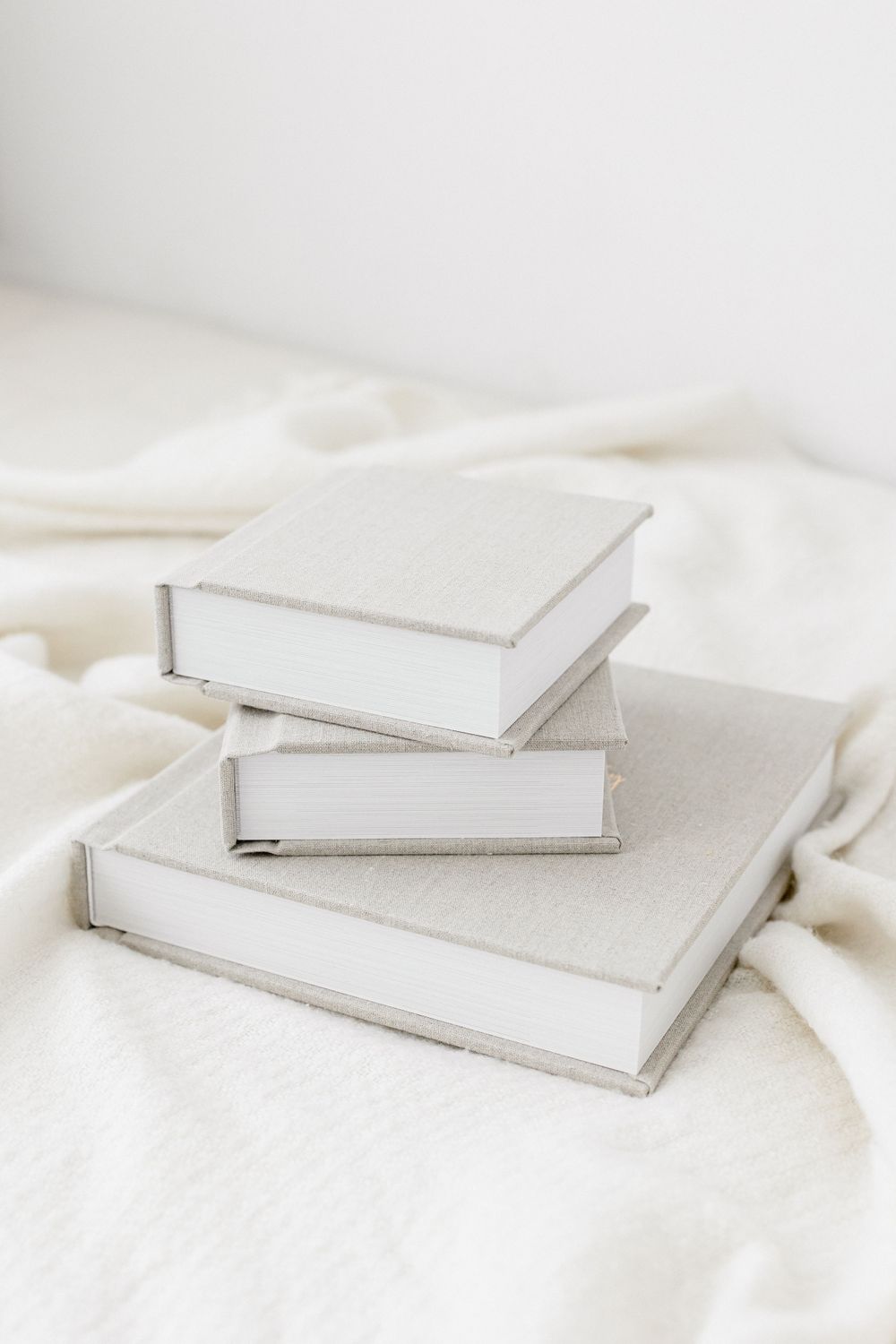 Minimalist white hardcover albums by Ashley Wilson, baby photographer in Jacksonville, arranged artistically on soft white fabric