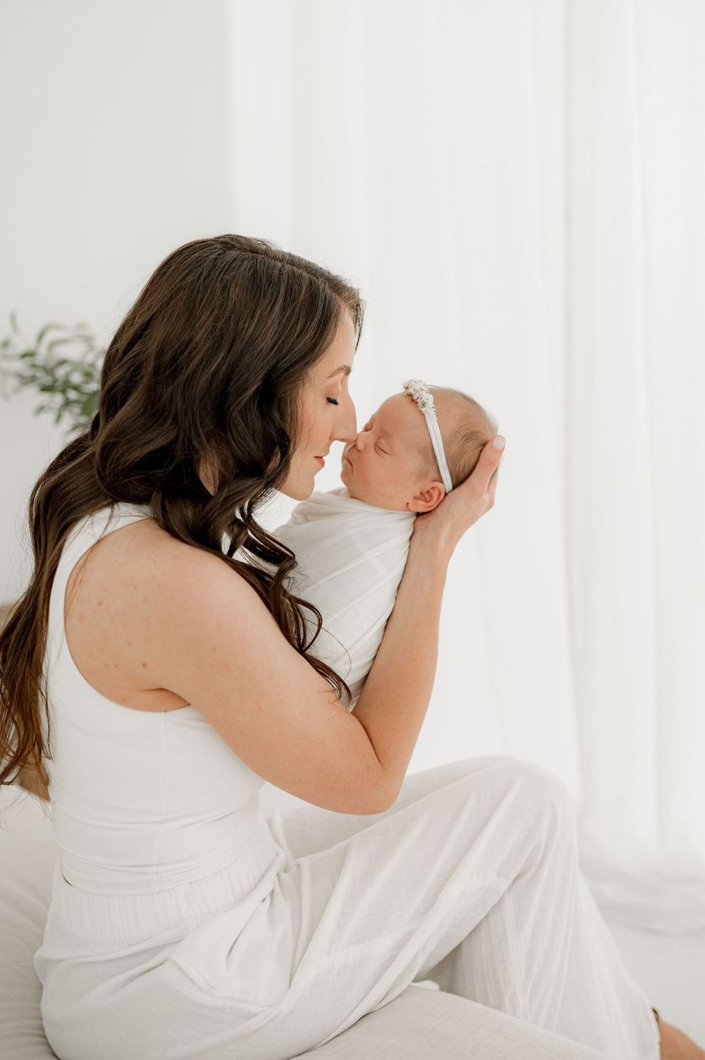 New mom in white clothing holding newborn baby up to her face for infant photography in Jacksonville FL