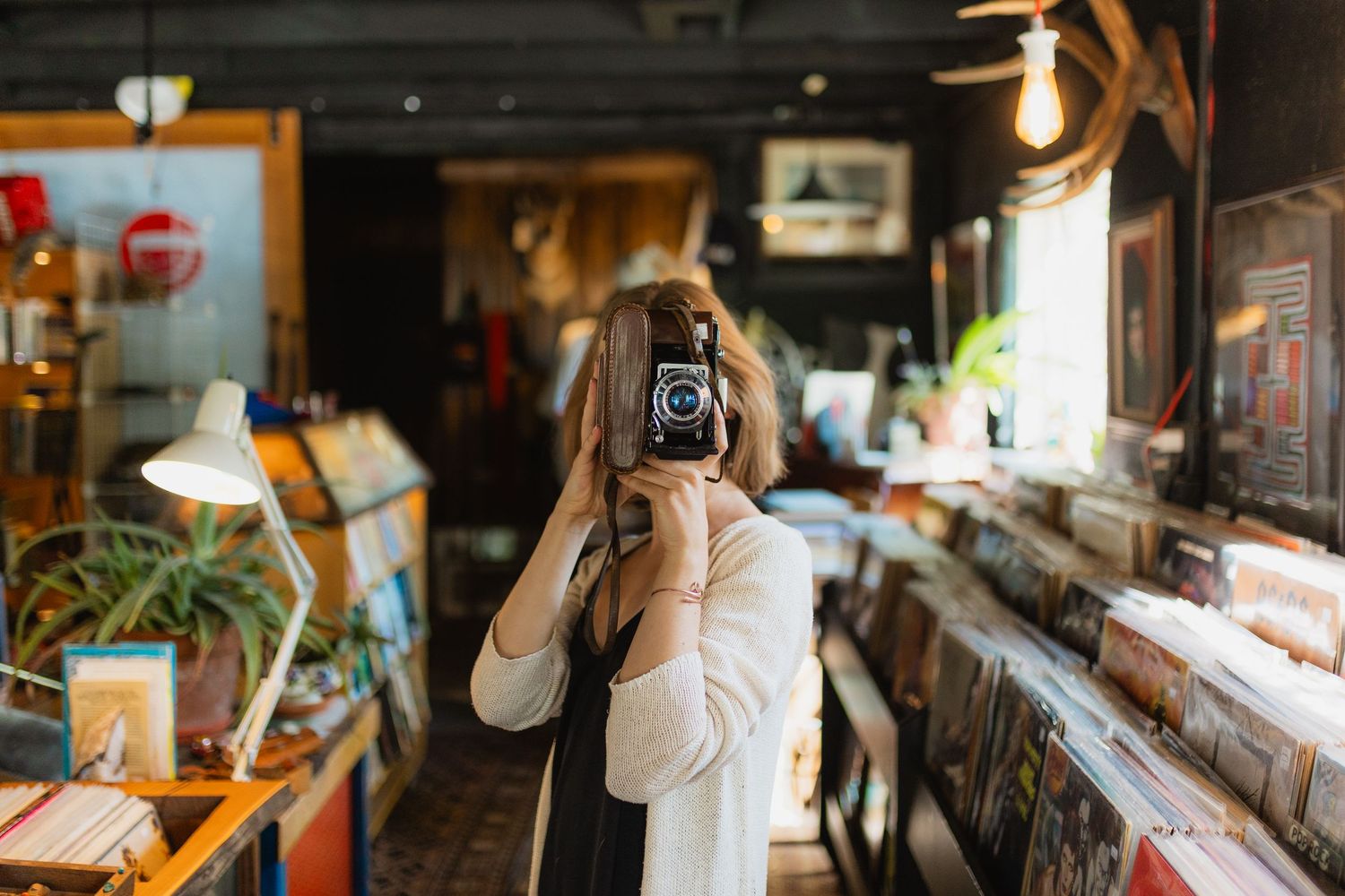 A person using a vintage film camera in a cozy record store filled with vinyl albums and retro decor.