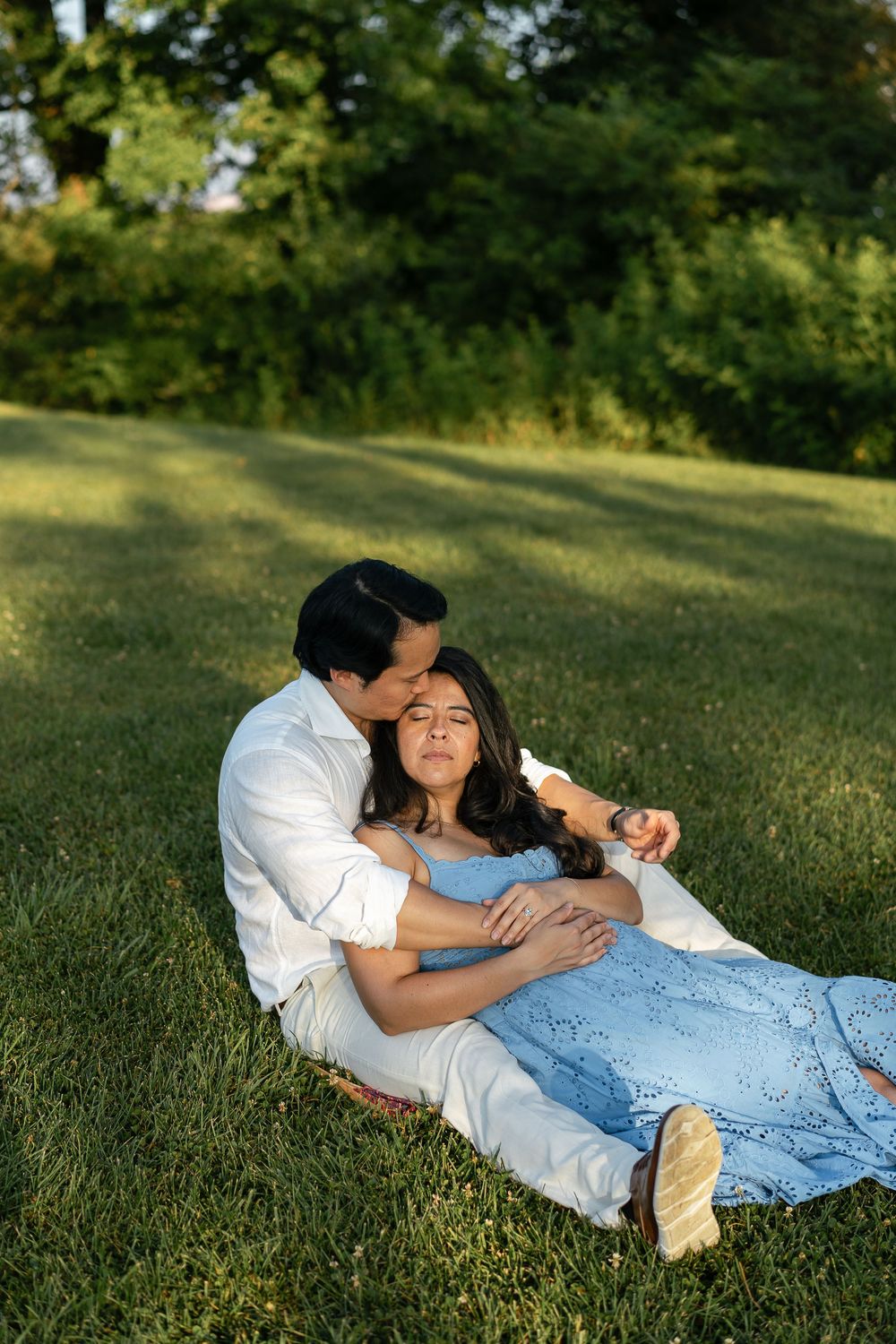 A romantic couple relaxes together on a sunny lawn during a golden hour photoshoot.