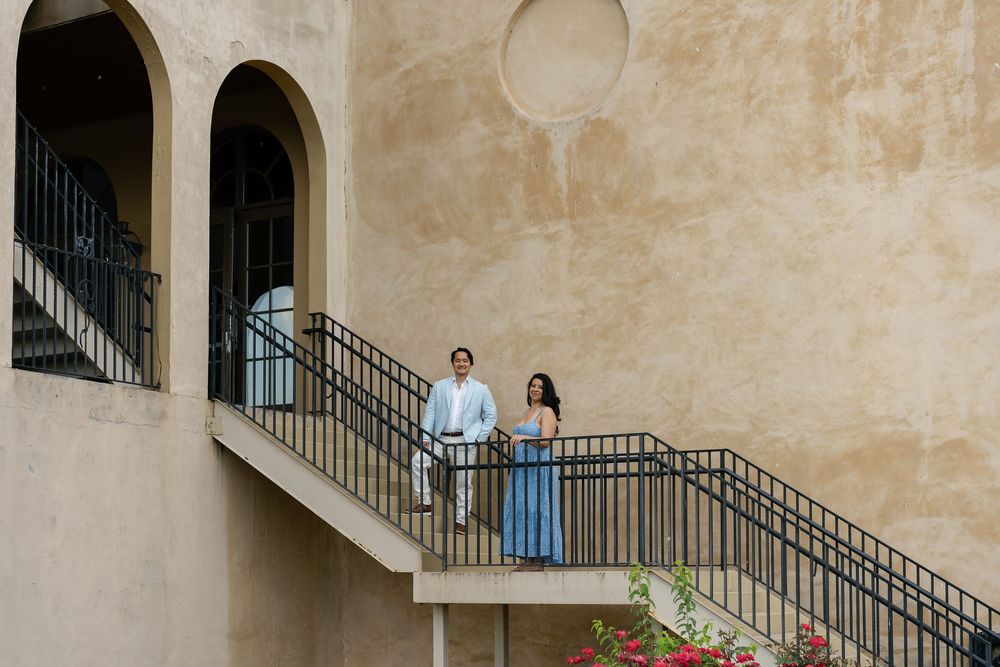 A stone spiral staircase curves around a center column in a historic building with people visible on upper levels.