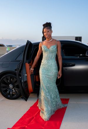 Smiling young woman in mint green mermaid gown exiting Rolls-Royce on red carpet.