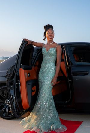 Young woman in mint green sequin mermaid gown posing beside black Rolls-Royce.
