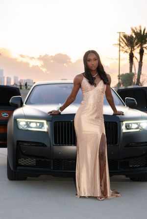 Woman in champagne sequin slit dress posing with black Rolls-Royce at dusk.