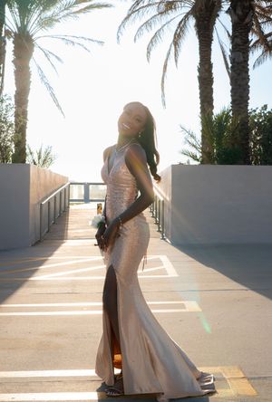 Young woman in rose gold sequin gown posing between palm trees at sunset.