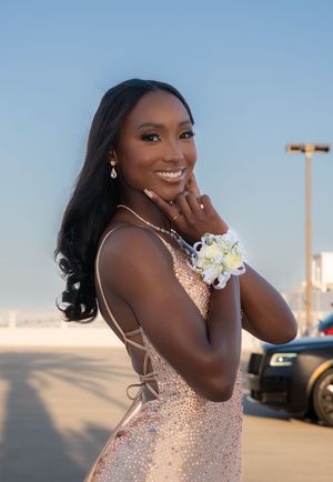 Smiling young woman in sequin prom dress wearing white wrist corsage outdoors.