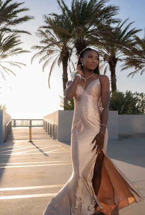 Young woman in rose gold sequin mermaid gown standing between palm trees at dusk.