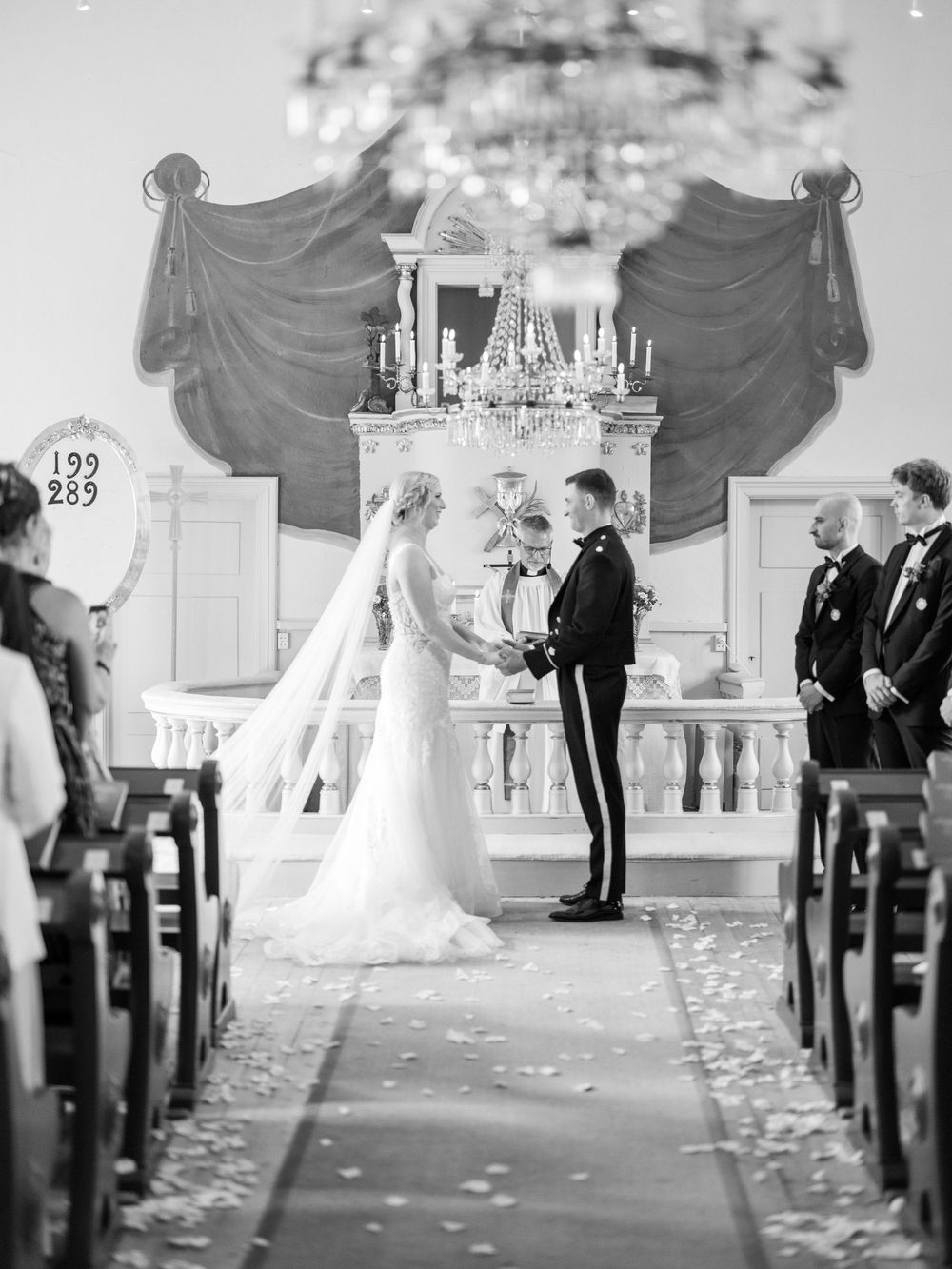 Black and white photo of an elegant church wedding ceremony with flower petals scattered along the aisle.