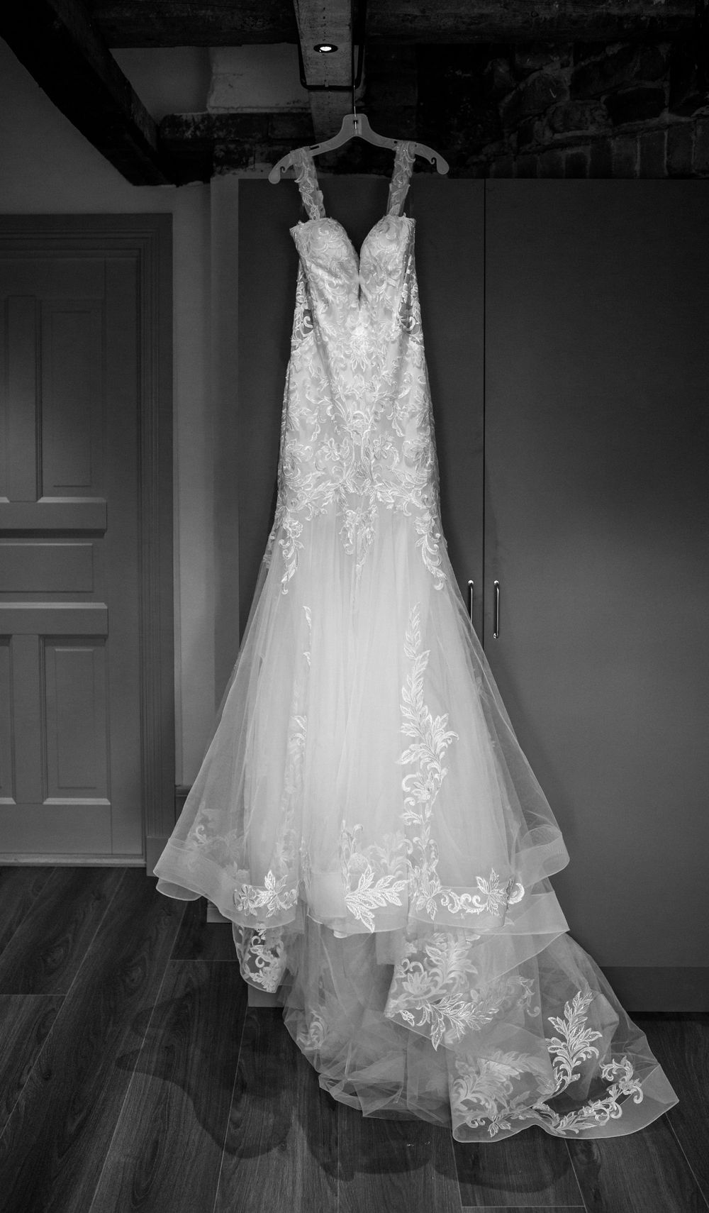 Elegant white wedding dress with lace appliques and tulle train hanging on display against grey wall.