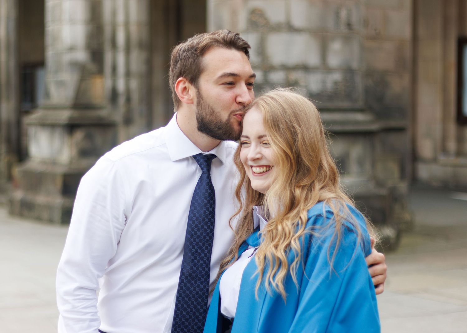 Graduates in bright blue gowns celebrate during a commencement ceremony at a historic stone building.