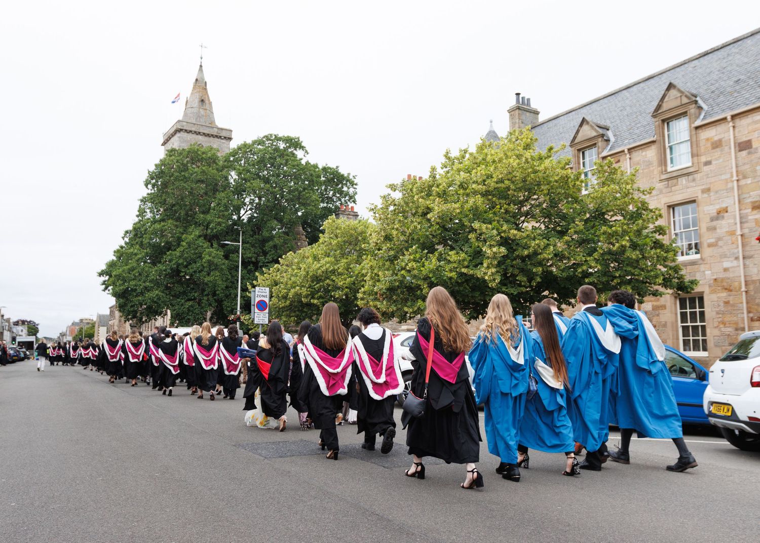 A line of graduates in academic regalia standing outside a stone building during a commencement ceremony.