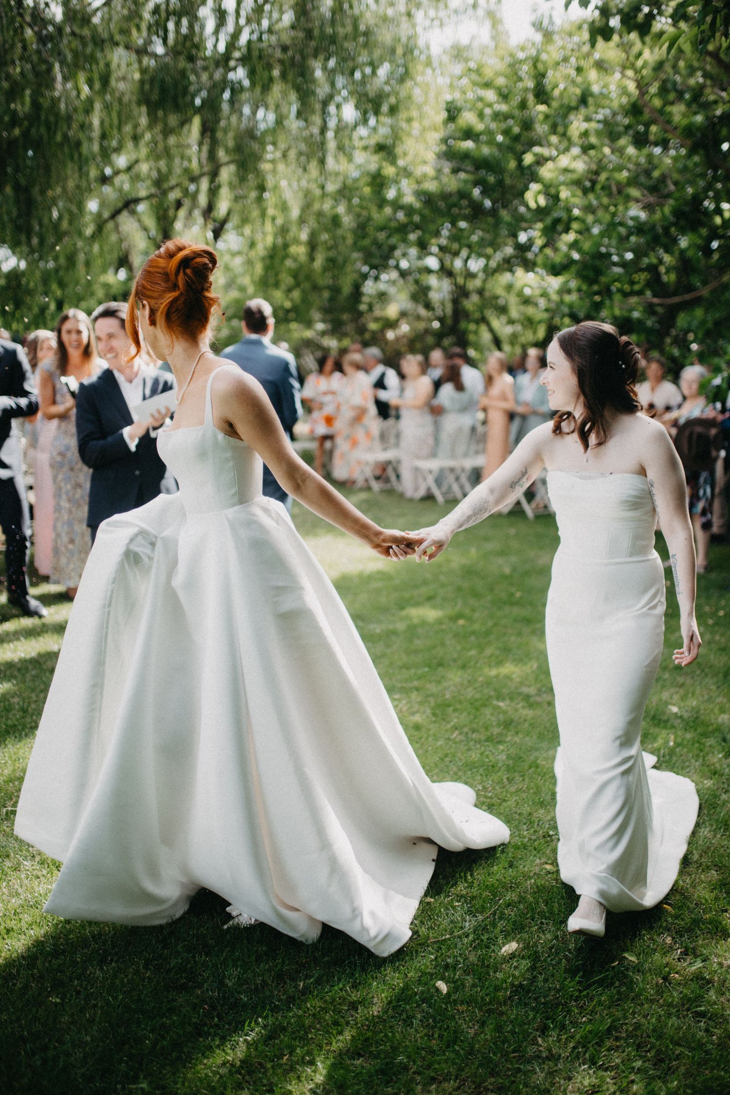 Wedding party in white dresses dances and twirls on a sunny lawn.