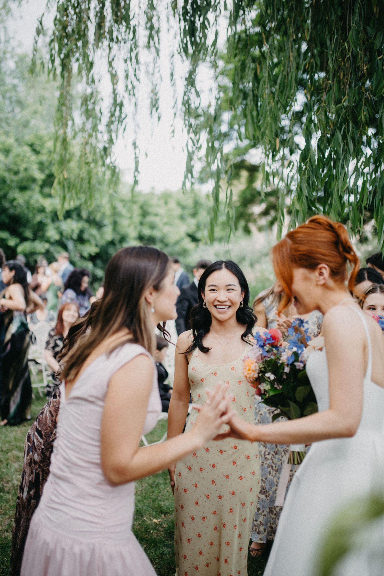 Wedding guests and bridal party share joyful moments under a weeping willow tree.