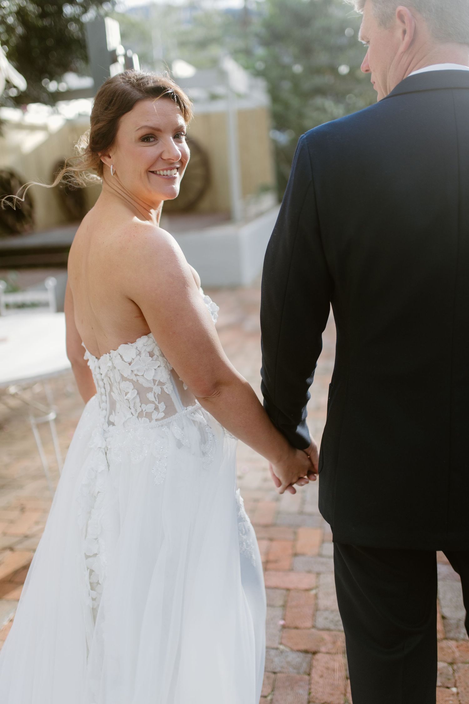 A couple walks hand in hand, with the bride wearing a beautiful lace back wedding gown.