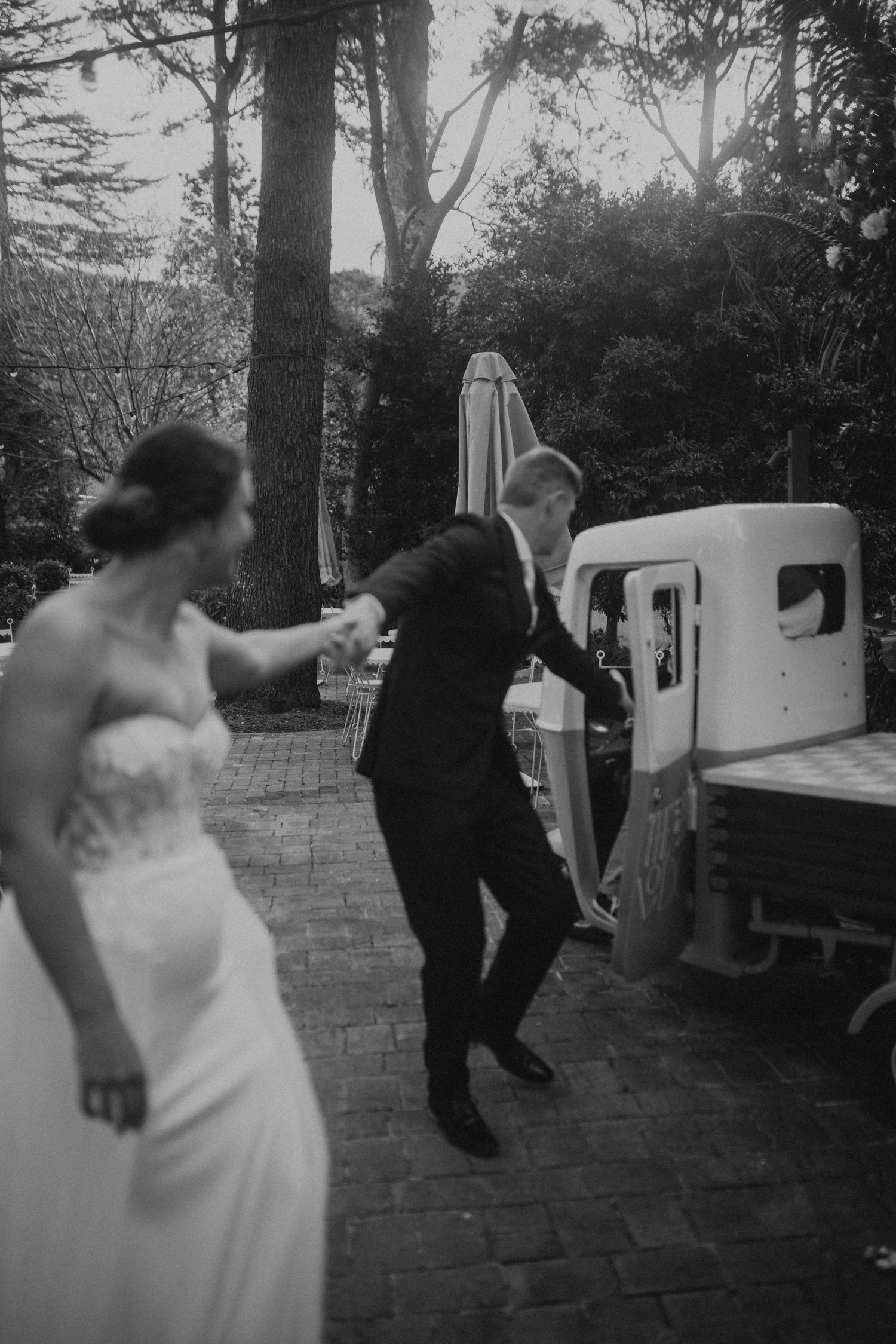 Black and white sequence shows a bride and groom dancing playfully on brick pavement.