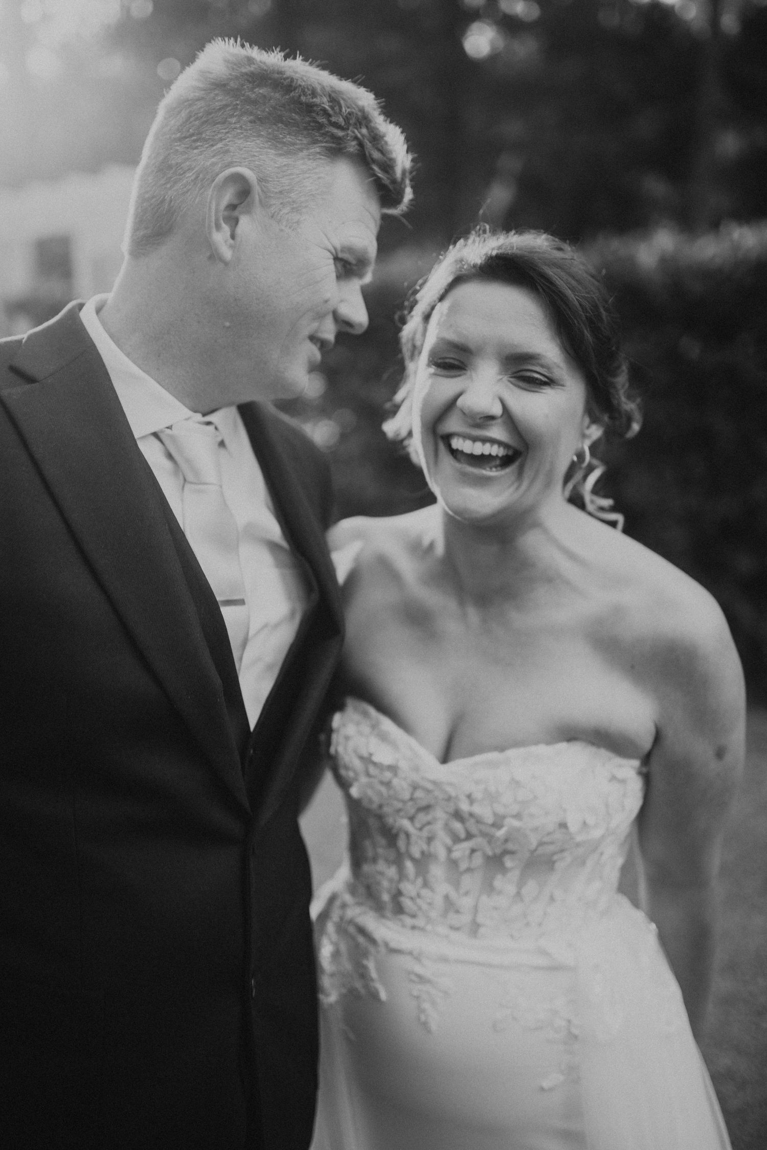 Black and white portrait captures intimate laughing moments between newlyweds.