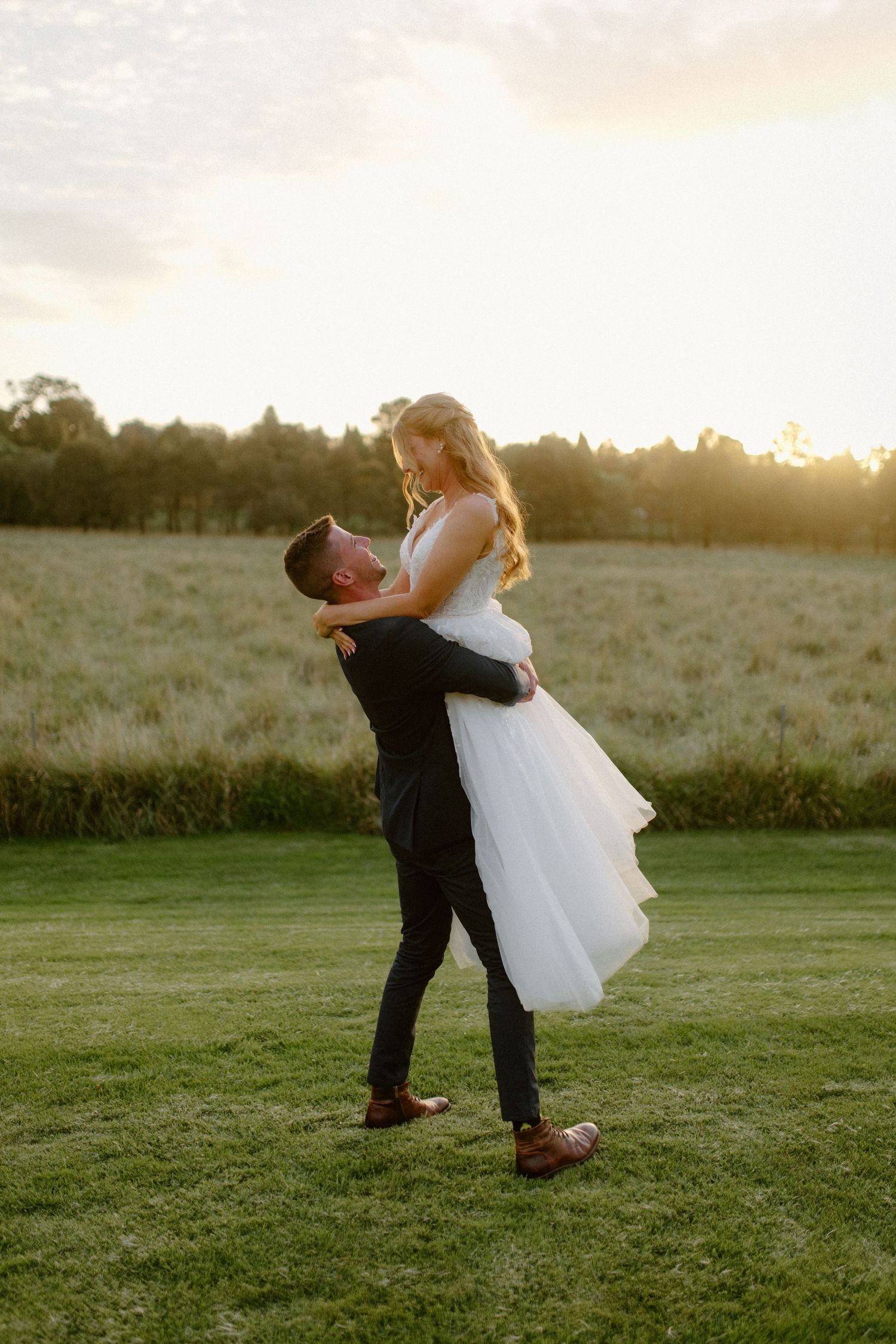 Romantic sunset wedding photos show couple embracing in a grassy field.