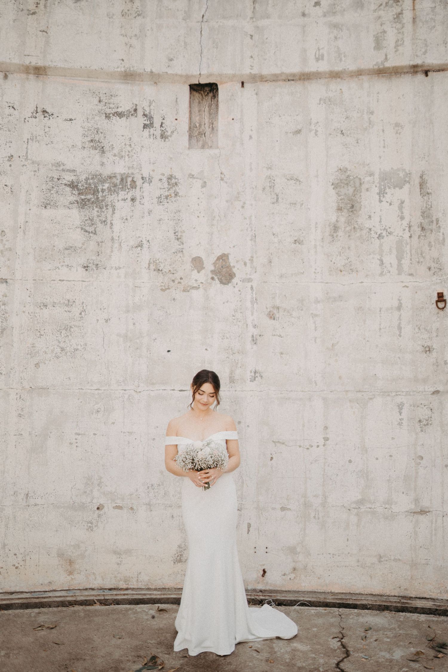 Artistic bridal portraits against weathered concrete wall showcasing elegant white wedding gown.