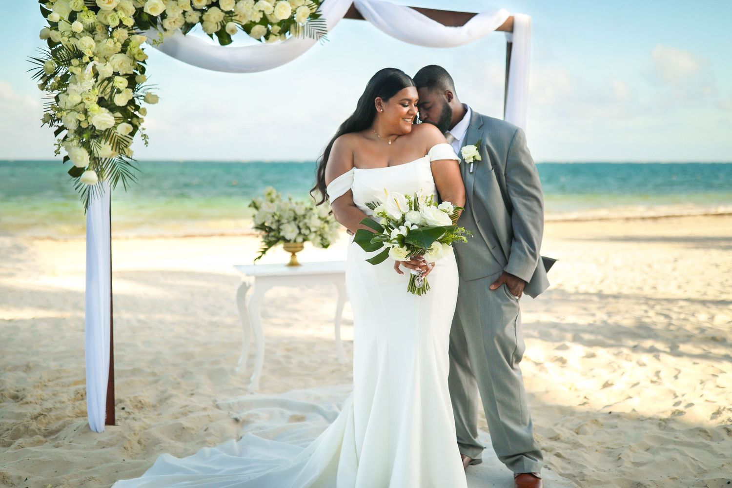 A romantic beach wedding ceremony under a floral arch with ocean waves in the background.