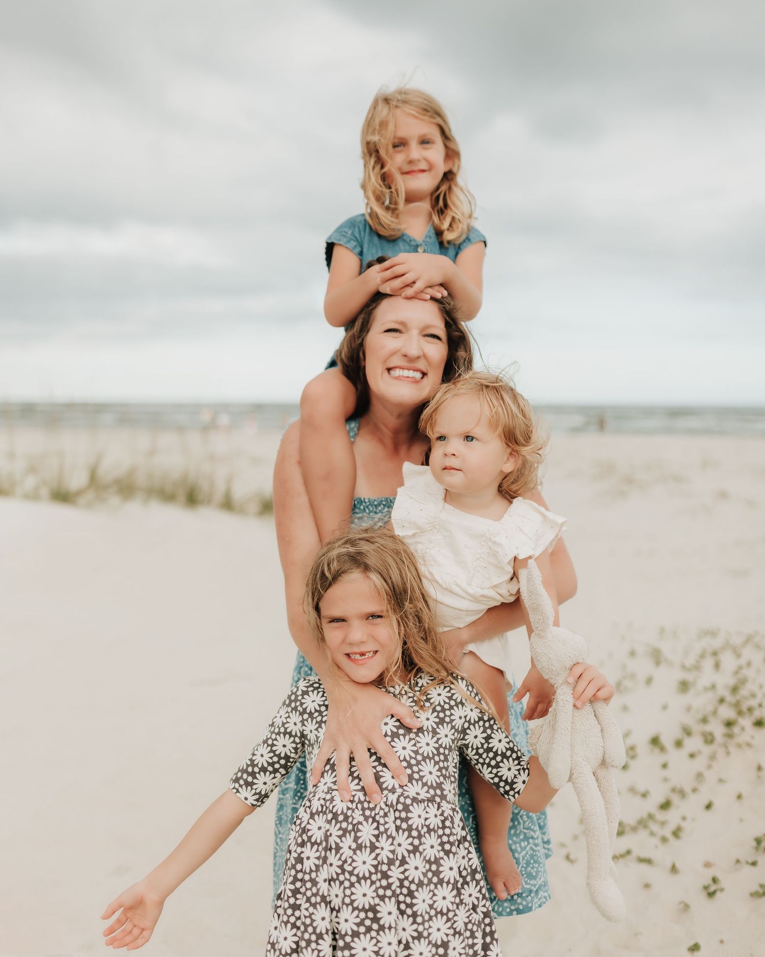 A joyful family moment unfolds as they dance and play together on sandy beach dunes under cloudy skies.